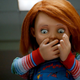 The Chucky doll from Child's Play holds his hands over his mouth in a scene from his TV series.